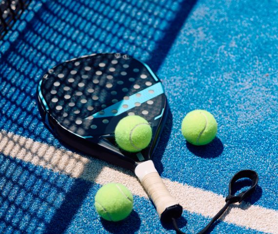 Paddle tennis racket and balls on blue outdoor court. Copy space.